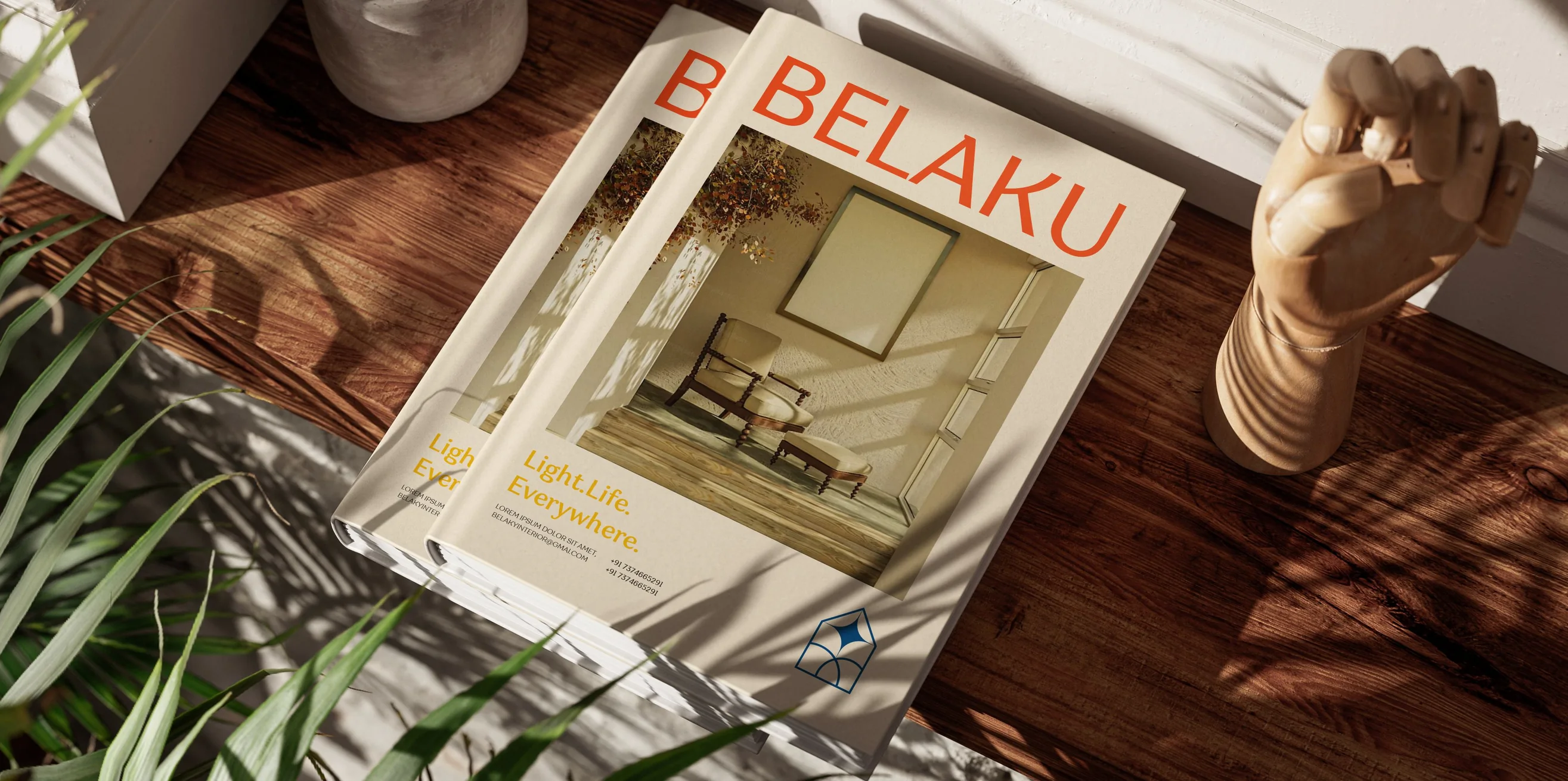 Two copies of the Belaku catalogue stacked on a wooden floor in raking sunlight, the terracotta wordmark and the Light. Life. Everywhere. line on the cover.