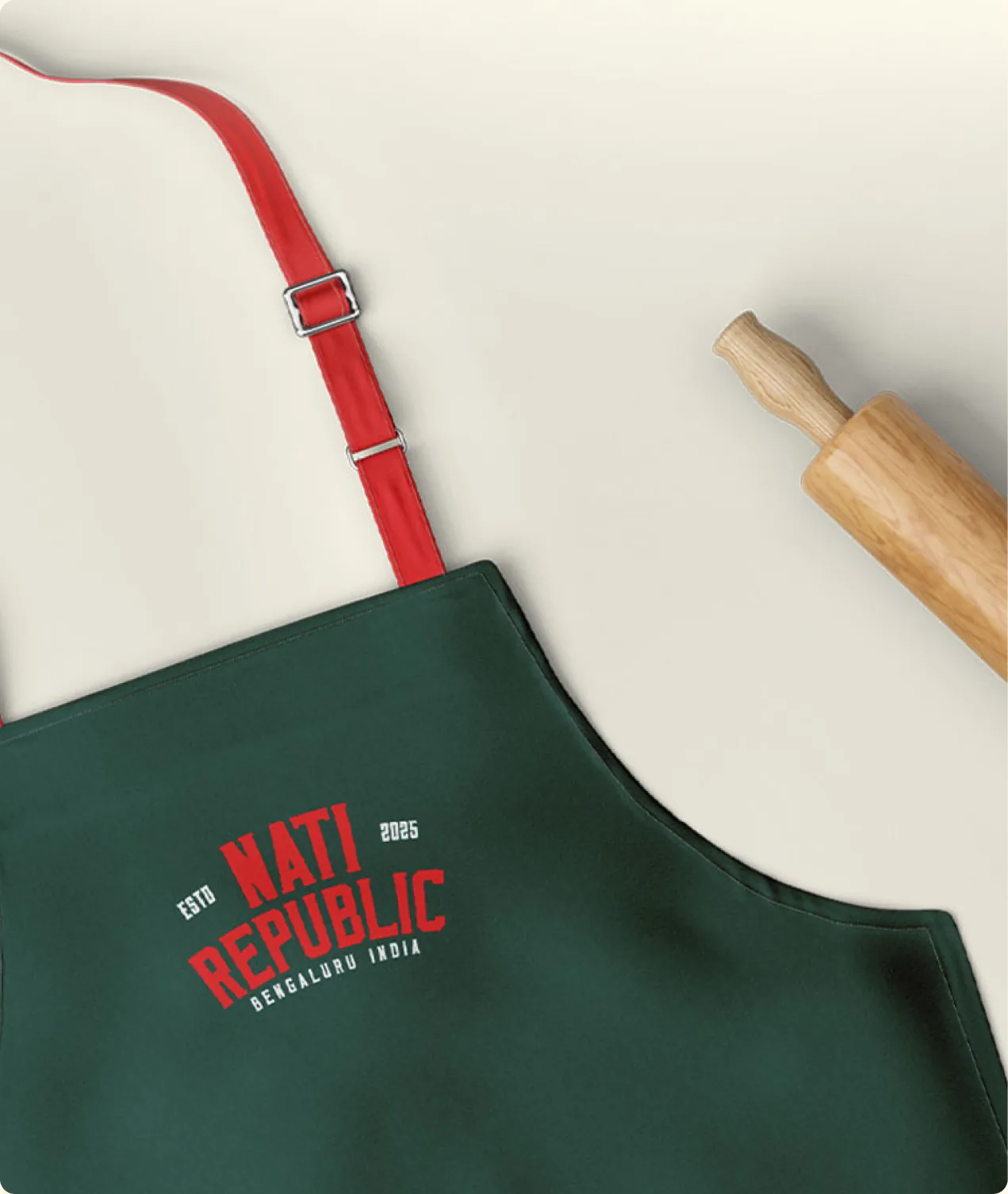 A green Nati Republic apron laid flat beside a rolling pin.