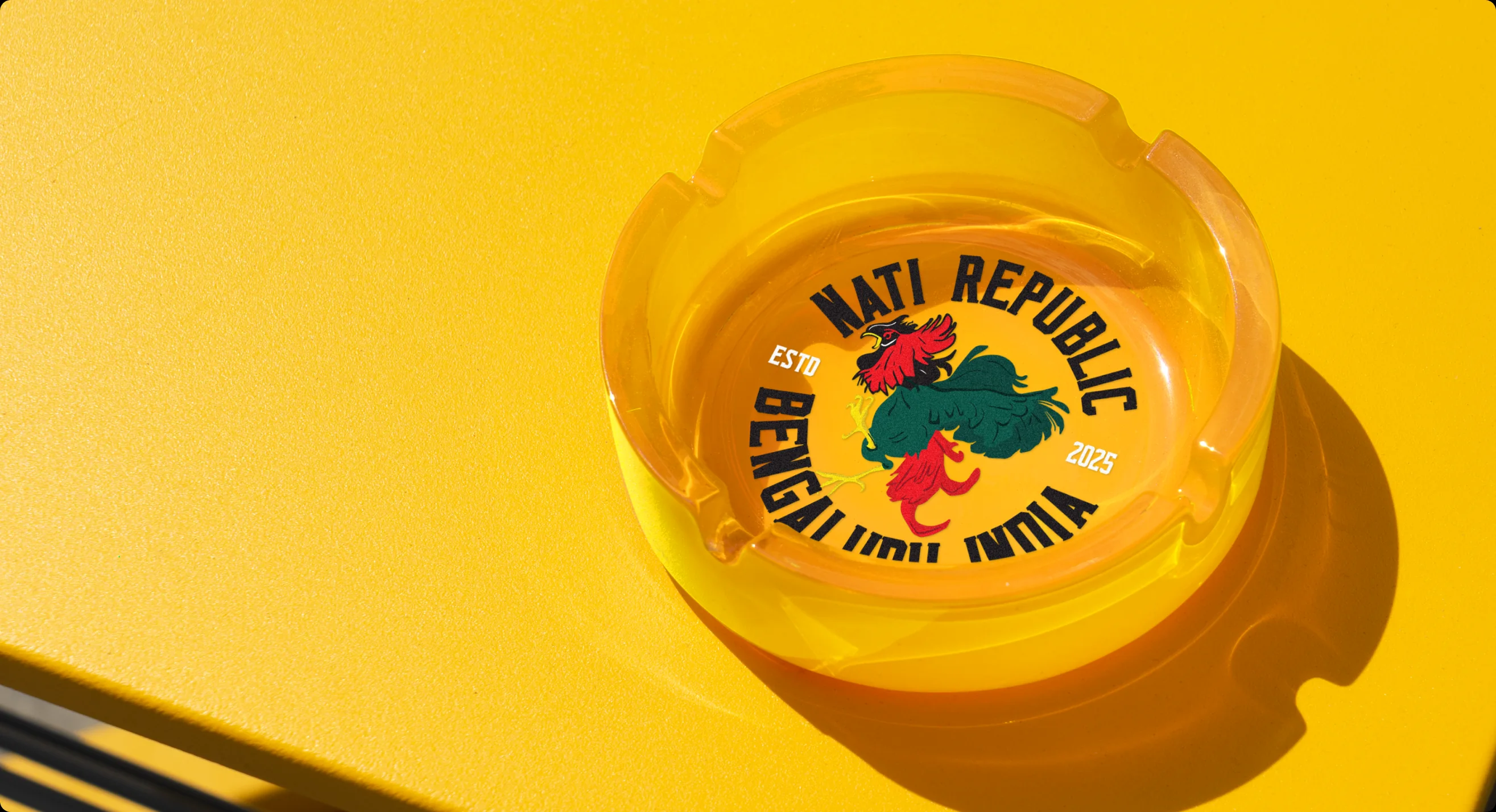 A yellow glass ashtray printed with the Nati Republic circle badge, on a yellow table.