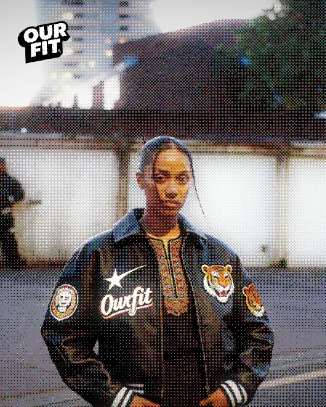 A woman in a black varsity jacket with an ourFIT script and tiger patches.